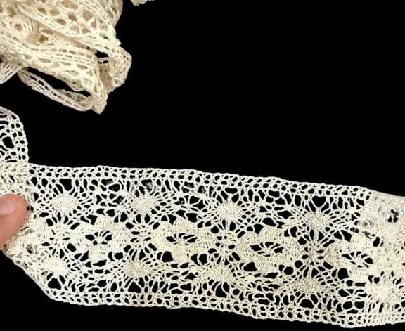 A length of crocheted cotton lace trim held up to the light.