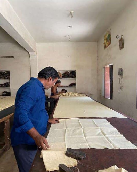 An artisan laying out fabric along a long printing table.