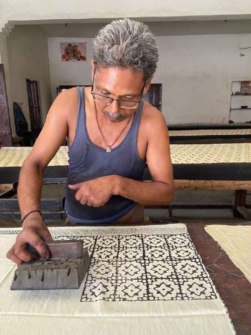 A printer pressing a carved block onto cloth, building a black-and-white repeat.