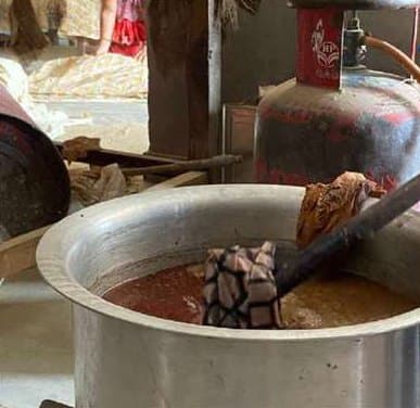 Printed fabric stirred in a pot of dye beside a gas cylinder.