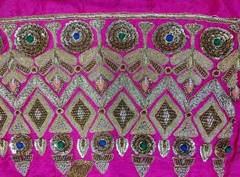 Dense gold dabka and mirror work in a geometric border on magenta.