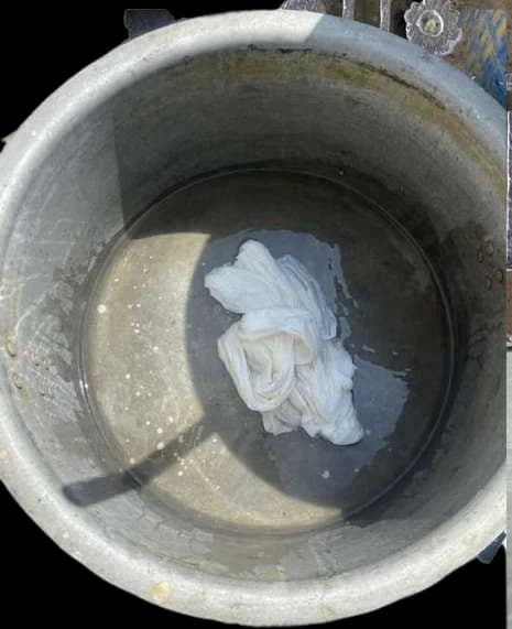 A white cloth soaking in a steel pot of water.