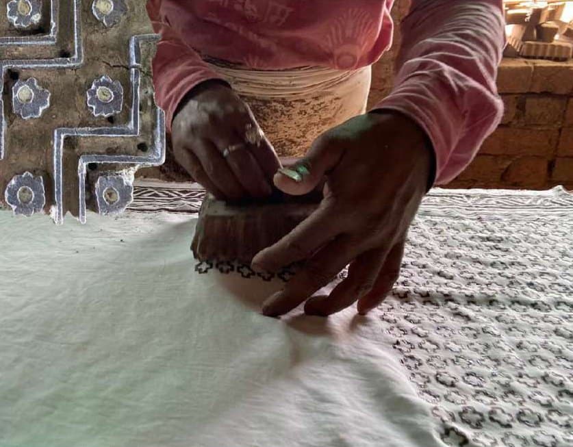 Hands pressing a mud-resist block onto white cloth.