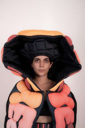 Final garment: a coral puffed cape with an oversized quilted hood.