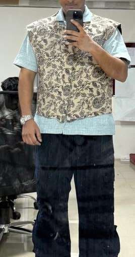 A mirror photo of a block-printed floral vest over a pale blue shirt, in the studio.