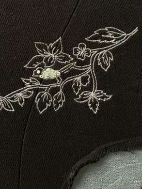 Close-up of white zari embroidery: a bird perched among leaves.
