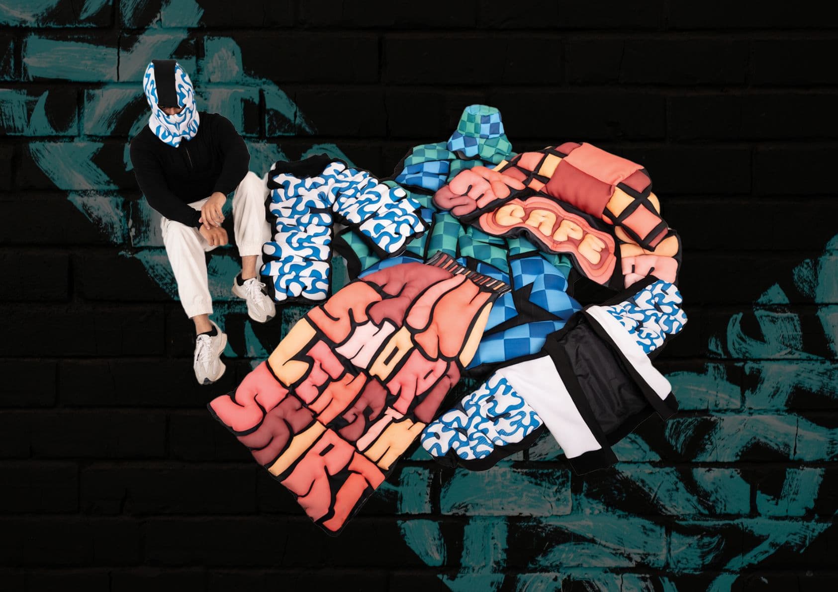 All three final garments laid out together on the graffiti wall, with Steve seated beside them wearing the balaclava.